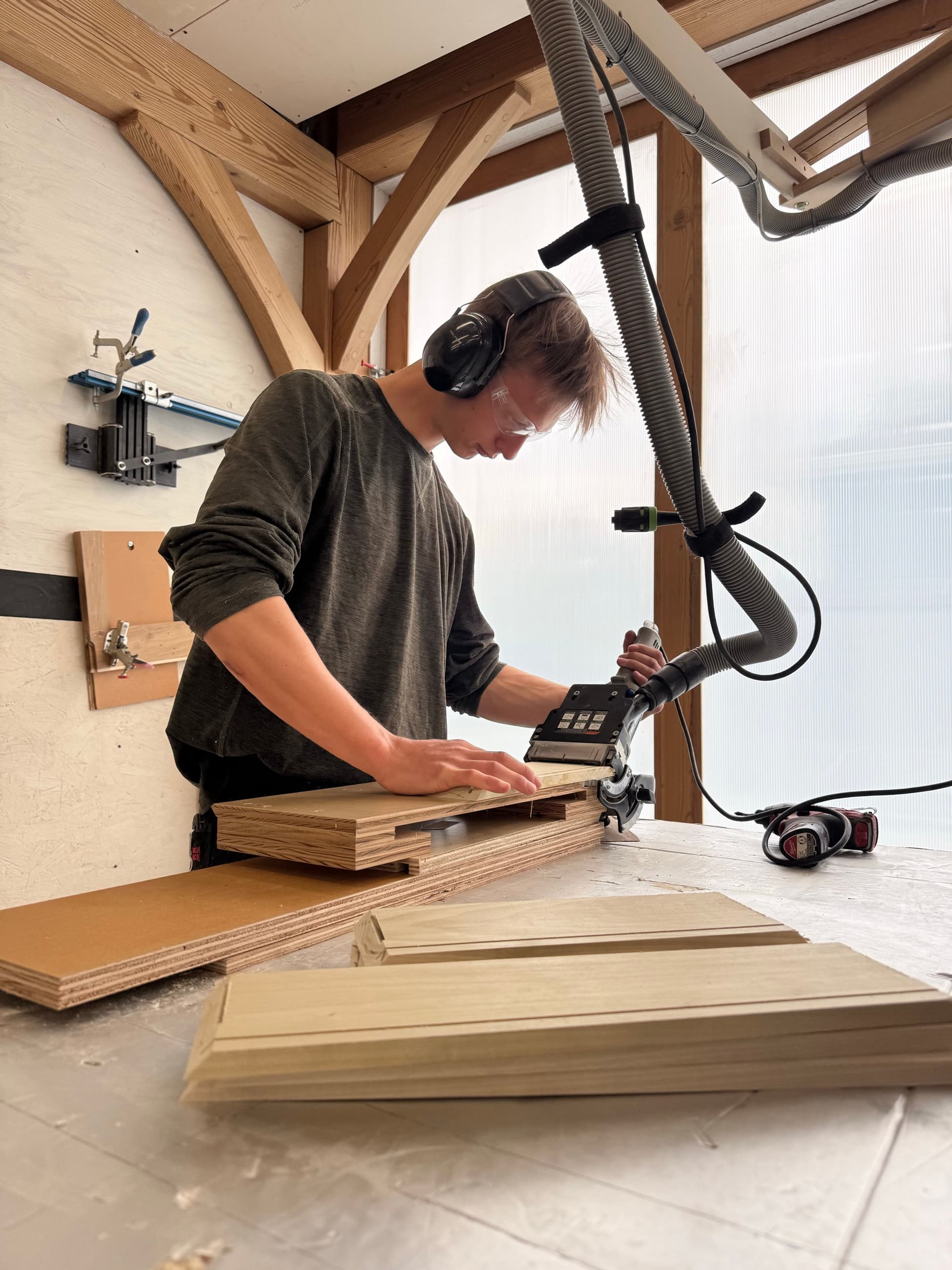 Aidan Gilbert routing cabinet parts in the shop with hearing and eye protection